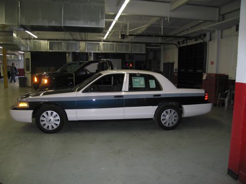 1991 Ford LTD Crown Victoria - black-over-white Ford Crown Victoria police sedan sits in profile inside a fleet maintenance garage with a paper placard in its window.