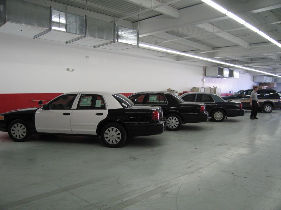 Row of black and white police sedans parked in a large indoor fleet garage