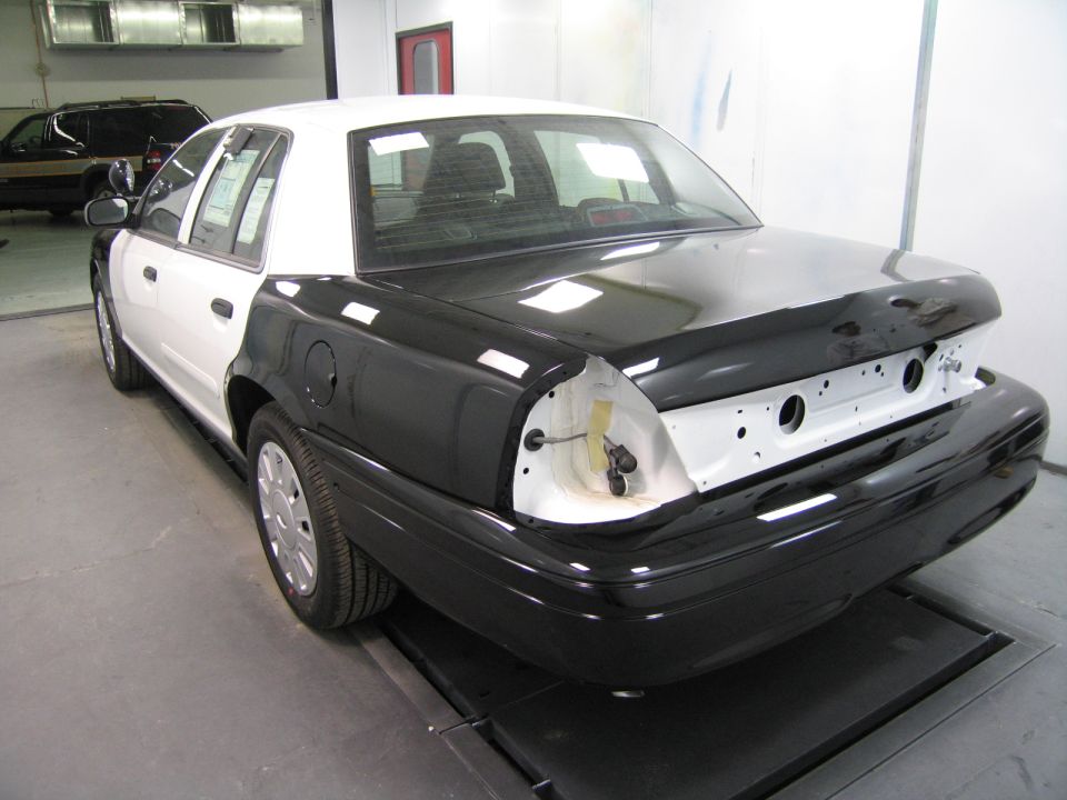 Rear of a black and white sedan with trunk and bumper removed in a paint booth