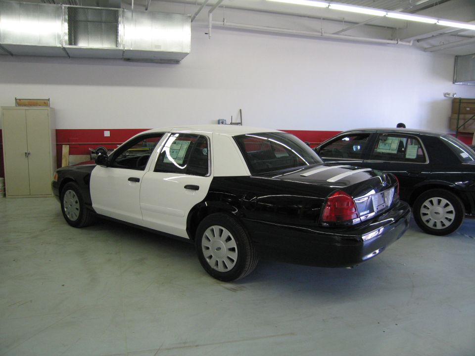 Freshly painted black and white police sedan parked indoors beside a dark sedan