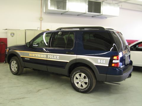 1991 Ford LTD Crown Victoria - dark blue Ford Explorer SUV lettered "Northwood Police" with "911" on the rear stands in a service garage.