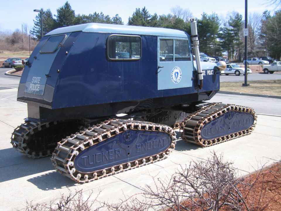 Blue tracked snow vehicle lettered State Police parked on a curb outdoors