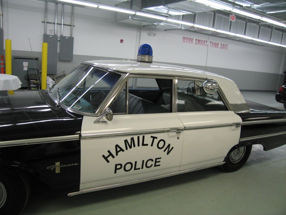 Black and white 1960s Ford Hamilton Police sedan with roof beacon indoors