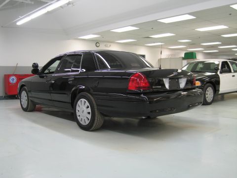 1991 Ford LTD Crown Victoria - glossy black Ford Crown Victoria sedan sits at a rear three-quarter angle in a clean shop beside a white police sedan.
