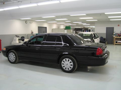 1991 Ford LTD Crown Victoria - black Ford Crown Victoria sedan sits in left profile on a clean shop floor with gray equipment lining the wall behind.