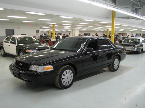 1991 Ford LTD Crown Victoria - black Ford Crown Victoria sedan with a Ford grille badge sits at a front three-quarter angle among other vehicles and workers in a shop.