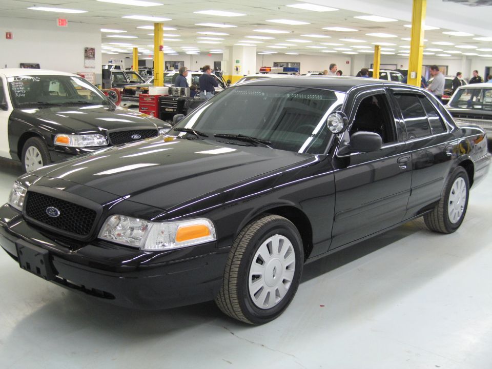 Black Ford Crown Victoria sedan with spotlight parked in a large shop