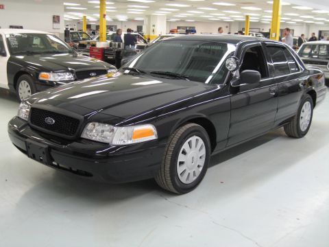 1991 Ford LTD Crown Victoria - black Ford Crown Victoria sedan with a spotlight sits at a front three-quarter angle in a busy shop next to a white police sedan.