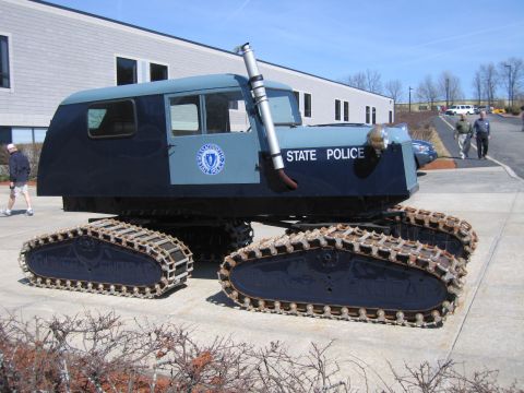 1991 Ford LTD Crown Victoria - two-tone blue tracked snow vehicle marked STATE POLICE with a chrome exhaust stack is parked on a paved lot near a building.