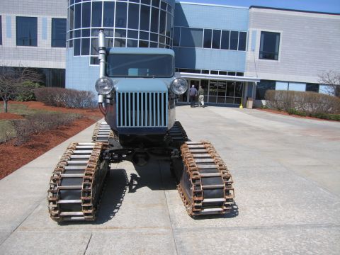 1991 Ford LTD Crown Victoria - front of a gray tracked snow machine showing twin round headlights, a vertical grille and exhaust stack, parked on a paved plaza outside a…