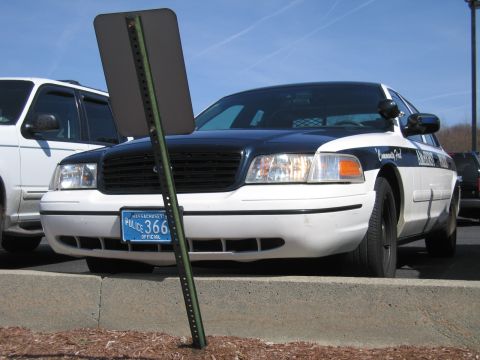 1991 Ford LTD Crown Victoria - Close front view of a black-and-white Ford police cruiser with a Massachusetts official plate reading POLICE 366, a sign post leaning acros…