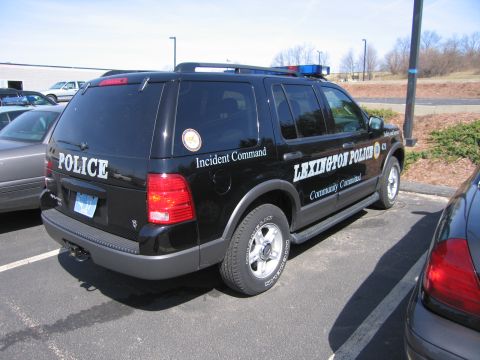 1991 Ford LTD Crown Victoria - black Ford Explorer lettered LEXINGTON POLICE, POLICE and Incident Command is parked in a lot, seen from the rear three-quarter.