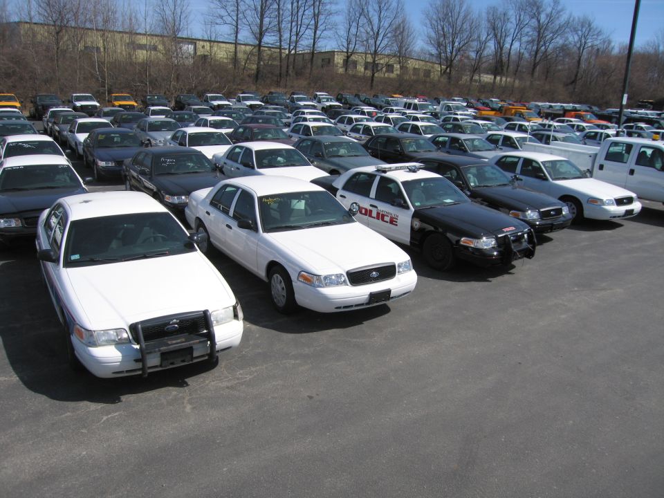 Rows of white and black police cruisers parked in a lot, one marked POLICE