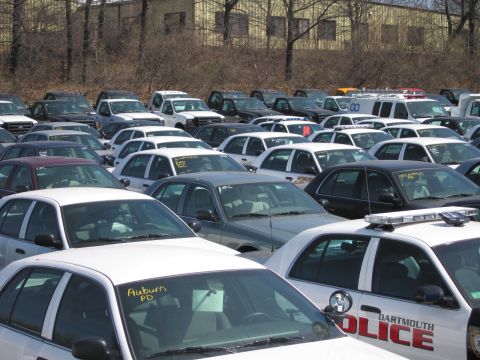 1991 Ford LTD Crown Victoria - crowded lot of police vehicles including a black-and-white DARTMOUTH POLICE cruiser and a sedan marked Auburn PD on its windshield.