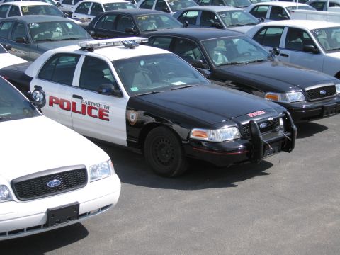 1991 Ford LTD Crown Victoria - black-and-white Ford Crown Victoria cruiser lettered DARTMOUTH POLICE with a roof light bar sits among rows of parked cars.
