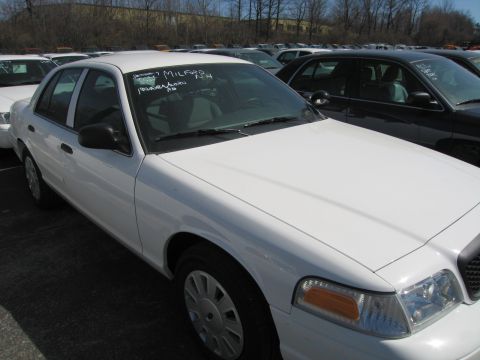 1991 Ford LTD Crown Victoria - white Ford Crown Victoria sedan with mileage and notes grease-penciled on its windshield is parked among other cars.