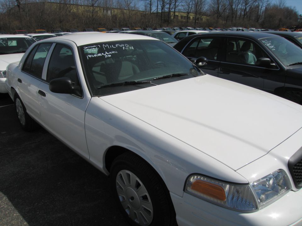 White Ford Crown Victoria sedan with mileage written on windshield in a lot