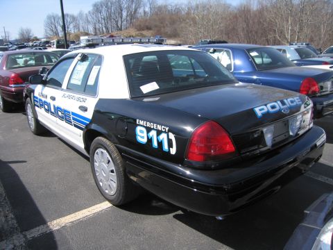1991 Ford LTD Crown Victoria - Rear three-quarter view of a black-and-white police Ford sedan with 'EMERGENCY 911' and 'POLICE' lettering, parked among other cruisers.