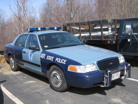 1991 Ford LTD Crown Victoria - two-tone blue Ford State Police sedan numbered 491 with push bar and light bar, parked beside a flatbed truck.