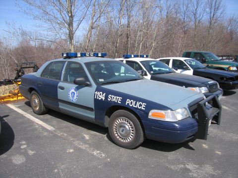 1991 Ford LTD Crown Victoria - two-tone blue Ford State Police sedan numbered 1194 with light bar and push bar parked in a lot near a green pickup.