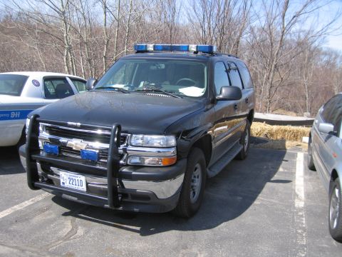1991 Ford LTD Crown Victoria - black Chevrolet full-size police SUV with brush guard, blue light bar and 22110 plate, parked in a lot beside a cruiser.