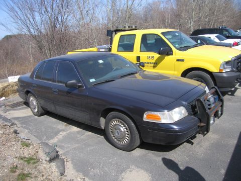 1991 Ford LTD Crown Victoria - dark blue unmarked Ford police sedan with front push bar parked beside a yellow MassPike pickup truck numbered 1815.