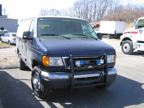 1991 Ford LTD Crown Victoria - dark blue Ford Econoline van with chrome brush guard and 'Wellesley PD' soaped on the windshield, parked in a lot.