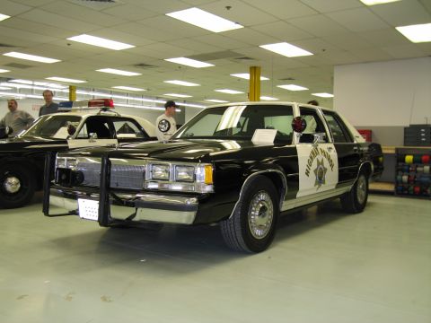 1991 Ford LTD Crown Victoria - black-and-white vintage California Highway Patrol Ford sedan with push bar and light bar displayed indoors with another cruiser behind.