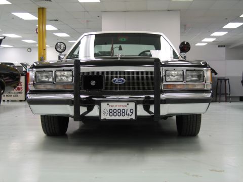 1991 Ford LTD Crown Victoria - Head-on front view of a dark vintage Ford sedan with push bar and California plate 888849 displayed on a showroom-style floor.