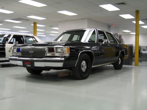 1991 Ford LTD Crown Victoria - Front three-quarter view of a black vintage Ford full-size sedan with chrome trim and red 'D.A.R.E.' front plate, displayed indoors.