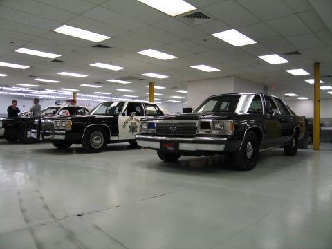 1991 Ford LTD Crown Victoria - black Ford LTD Crown Victoria police sedan sits beside a black-and-white Sheriff patrol car inside a brightly lit indoor collection.