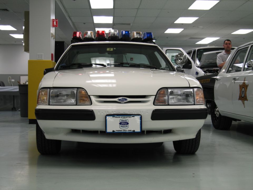 Front view of a white Ford Mustang police interceptor with roof light bar