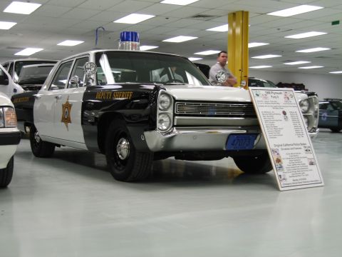 1991 Ford LTD Crown Victoria - black-and-white Plymouth Deputy Sheriff police sedan with a blue roof light sits on display beside a printed information placard.