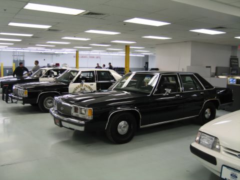 1991 Ford LTD Crown Victoria - black Ford LTD Crown Victoria police sedan is parked among other patrol cars inside a brightly lit indoor showroom.