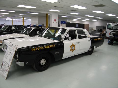 1991 Ford LTD Crown Victoria - black-and-white Plymouth Deputy Sheriff police sedan with twin roof spotlights is parked on display in an indoor collection.