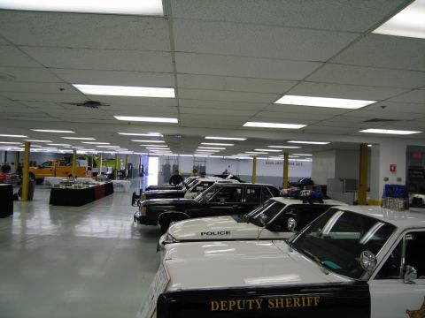 1991 Ford LTD Crown Victoria - long row of black-and-white police cruisers, including a Deputy Sheriff car, is lined up across a large indoor exhibition floor.