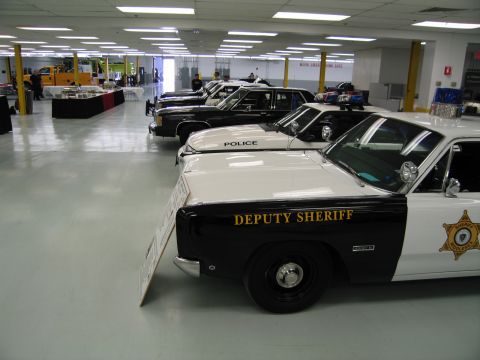 1991 Ford LTD Crown Victoria - line of police cars stretches across an indoor hall, led by a black-and-white Deputy Sheriff sedan in the foreground.