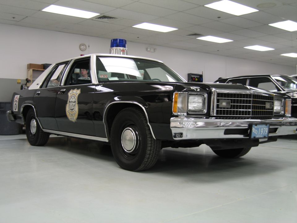Black-and-white Ford LTD police sedan with city police emblem indoors