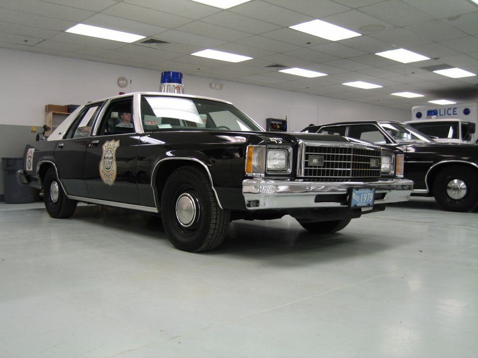Black-and-white Ford LTD police cruiser with gold door emblem indoors