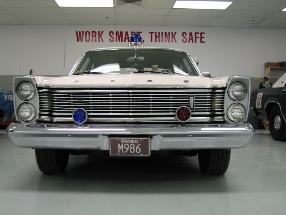 Front of a white 1960s Ford Galaxie police car under Work Smart Think Safe sign