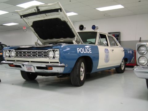 1991 Ford LTD Crown Victoria - blue-and-white Plymouth police car marked Police with its hood up and twin roof spotlights sits on display indoors.