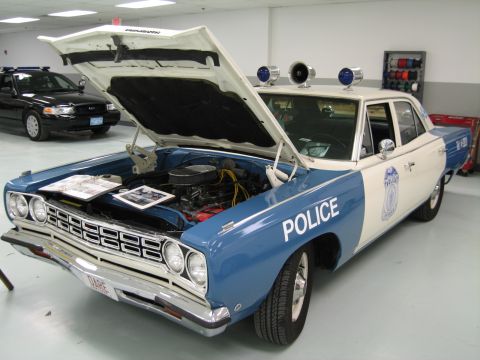 1991 Ford LTD Crown Victoria - blue-and-white Plymouth police car displays its engine bay with the hood raised and documents laid across it, indoors.