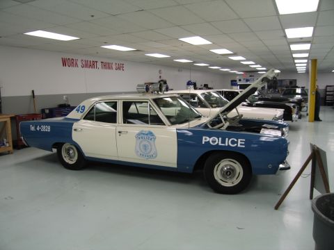 1991 Ford LTD Crown Victoria - blue-and-white police sedan numbered 49 with a police door emblem and raised hood sits below a Work Smart Think Safe wall sign.