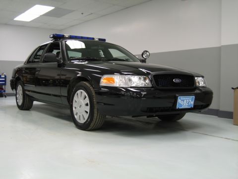 1991 Ford LTD Crown Victoria - black Ford Crown Victoria police interceptor with a blue roof light bar and spotlight sits in a clean indoor showroom.