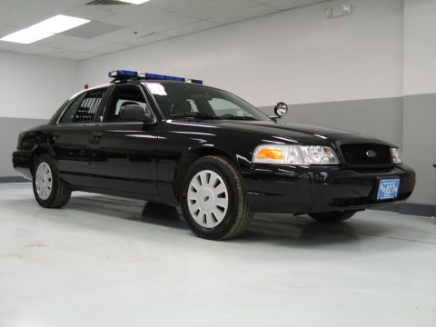 1991 Ford LTD Crown Victoria - black Ford Crown Victoria police interceptor with a blue roof light bar is shown in a three-quarter front view indoors.