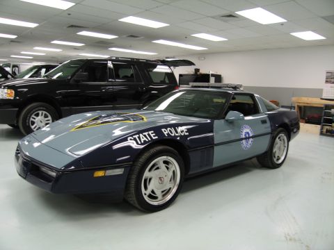1991 Ford LTD Crown Victoria - gray-and-blue Chevrolet Corvette marked State Police sits on display beside a black SUV in an indoor collection.
