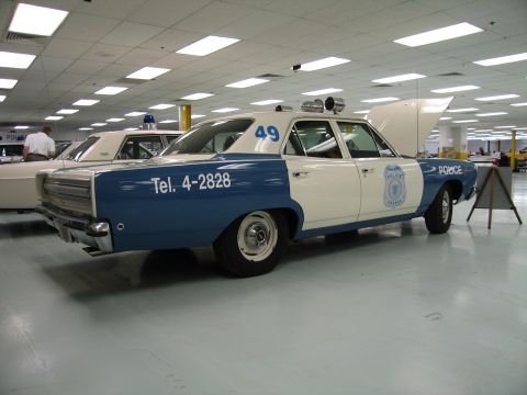 1991 Ford LTD Crown Victoria - rear quarter of a blue-and-white Plymouth police sedan numbered 49 with Tel. 4-2828 lettering is shown on the showroom floor.