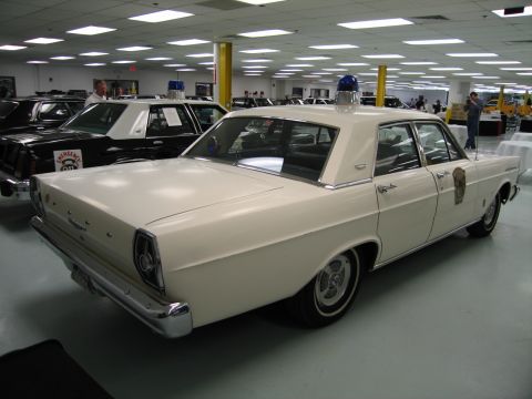 1991 Ford LTD Crown Victoria - rear three-quarter view of a white 1960s Ford Galaxie police sedan with a blue dome light sits among other cruisers indoors.