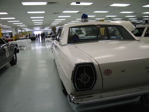 1991 Ford LTD Crown Victoria - white vintage Ford four-door with a blue roof beacon and red AAA emblem sits among other cars in an indoor display hall.