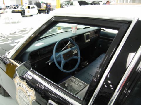 1991 Ford LTD Crown Victoria - Through an open window, the blue vinyl interior of a police car shows a steering wheel, dashboard and a Police shield on the door.